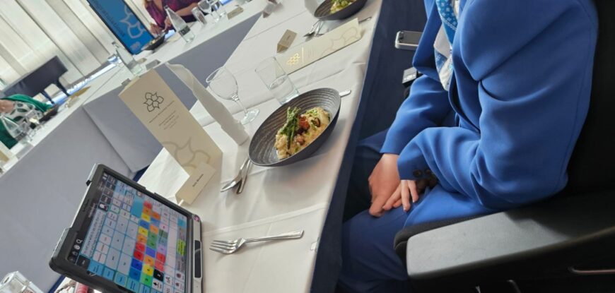 Person sat at a white covered table with a plate of food, drinks and an eye gaze device. Access is not just proximity to resources but seating, nutrition and hydration