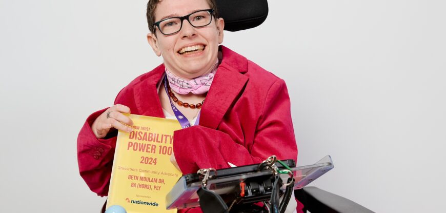 Beth Moulam wearing pink holding a yellow and red award. The disability Power 100 2024 Grass Roots and Community Advocate winner